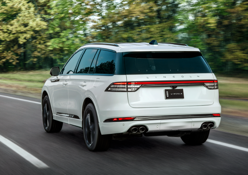 A white 2025 Lincoln Aviator® SUV is being driven away down a road lined with colorful trees. | Libertyville Lincoln Sales, Inc. in Libertyville IL