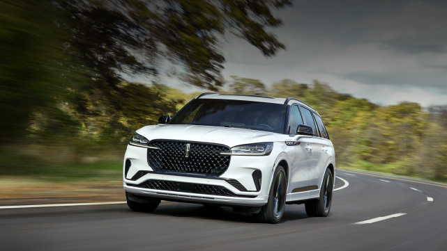 A white 2025 Lincoln Aviator® SUV is being driven down a road lined with trees. | Libertyville Lincoln Sales, Inc. in Libertyville IL