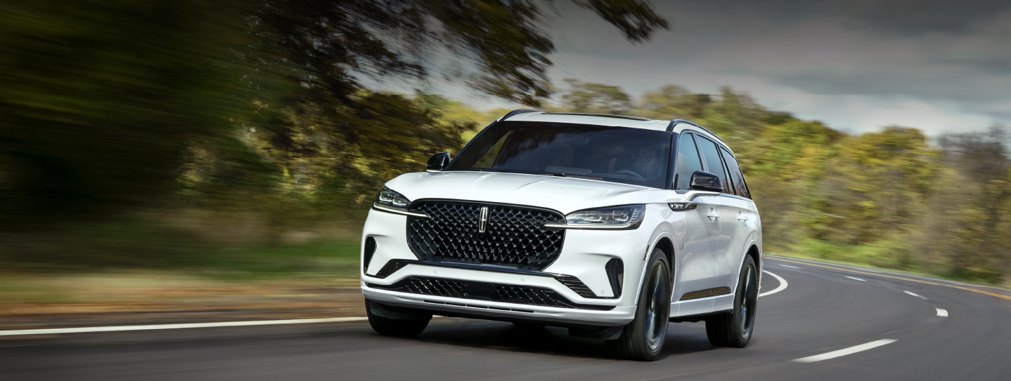 A white 2025 Lincoln Aviator® SUV is being driven down a road lined with trees. | Libertyville Lincoln Sales, Inc. in Libertyville IL