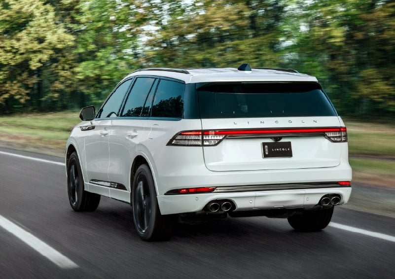A white 2026 Lincoln Aviator® SUV is being driven away down a road lined with colorful trees. | Libertyville Lincoln Sales, Inc. in Libertyville IL