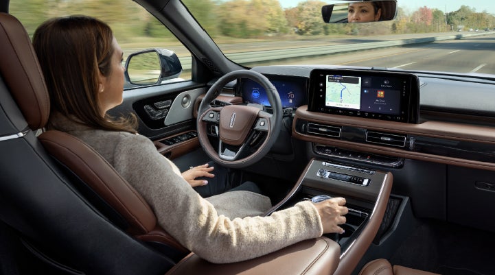 A 2027 Lincoln Aviator® SUV is being driven hands-free on a highway lined with trees. | Libertyville Lincoln Sales, Inc. in Libertyville IL