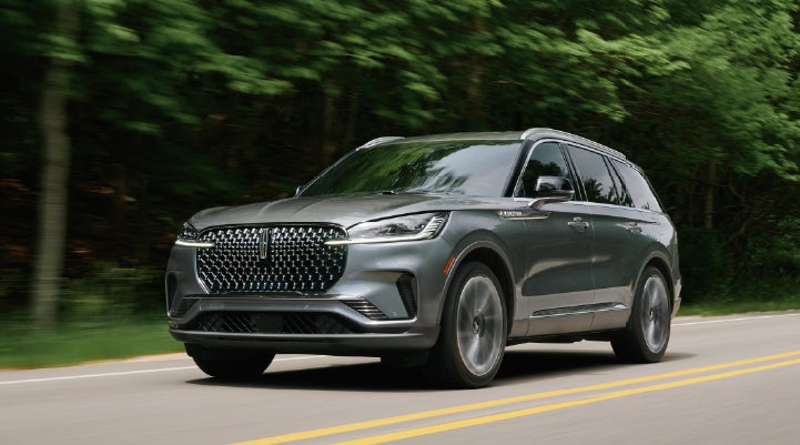 A 2027 Lincoln Aviator® SUV is being driven down a road lined with trees. | Libertyville Lincoln Sales, Inc. in Libertyville IL